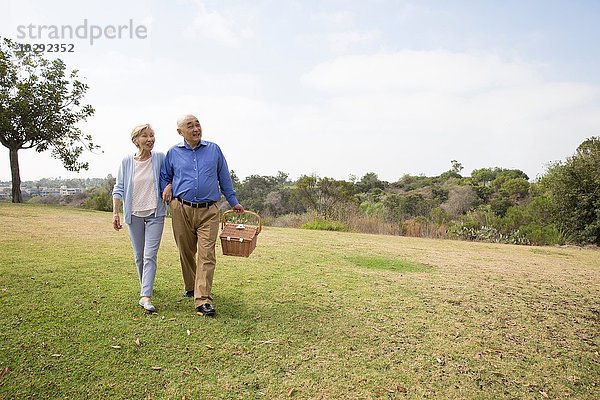 Seniorenpaar mit Arm in Arm im Park  Picknickkorb tragend