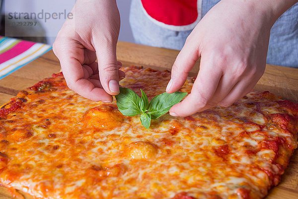 Hände der Frau  die Basilikum auf die Pizza an der Küchentheke legt.