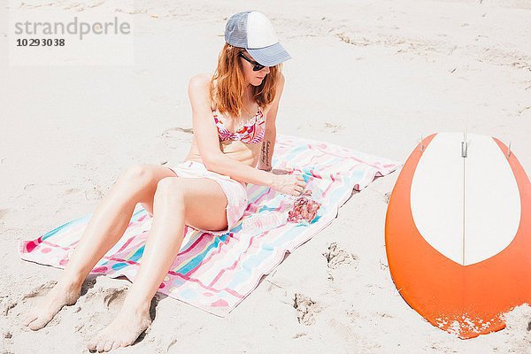 Mittlere erwachsene Frau am Strand  Trauben essen  Surfbrett neben ihr