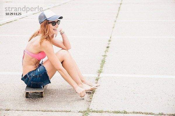 Mittlere erwachsene Frau auf dem Skateboard sitzend. Lachend.