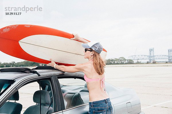 Mittlere erwachsene Frau am Strand  Entfernen des Surfbrettes vom Autodach