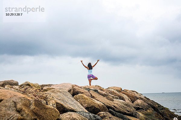 Rückansicht einer reifen Frau  die Yoga auf Küstenfelsen praktiziert  Cape Cod  USA