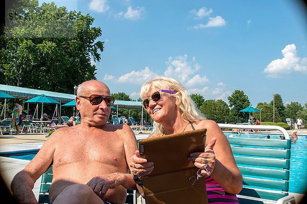 Seniorenpaar beim Betrachten des digitalen Tabletts im Freibad