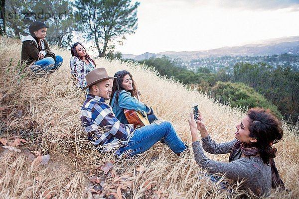 Junge Frau fotografiert ihre vier erwachsenen Geschwister auf einem grasbewachsenen Hügel.