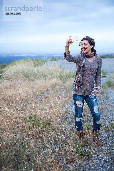 Junge Frau posiert für Smartphone Selfie auf ländlichem Hügel