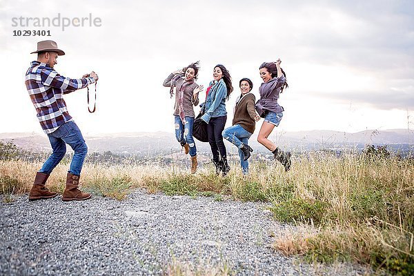 Junger Mann fotografiert seine vier erwachsenen Schwestern beim Sprung auf den Hügel