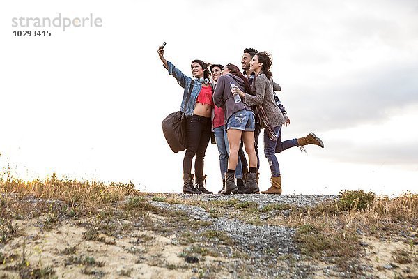 Junger Mann und vier erwachsene Schwestern posieren für Smartphone Selfie auf Schotterpiste