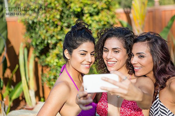 Drei erwachsene Schwestern in Bikini-Tops posieren für Smartphone Selfie im Garten