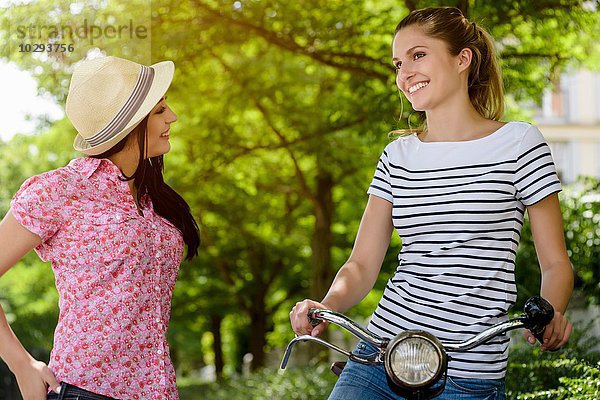 Junge Frau auf dem Fahrrad im Gespräch mit junger Frau mit Panamahut