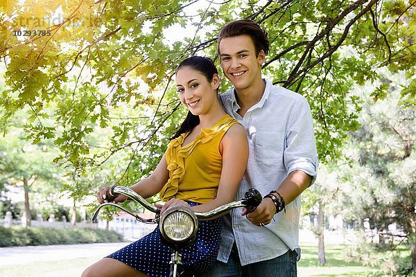 Junges Paar im Park mit Fahrrad und lächelndem Blick auf die Kamera