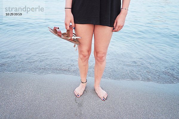 Taille unten von junger Frau am Strand mit Sandalen
