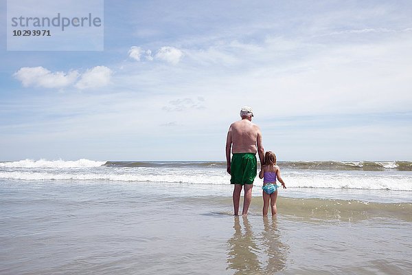 Rückansicht eines älteren Mannes  der mit seiner Enkelin im Meer paddelt.