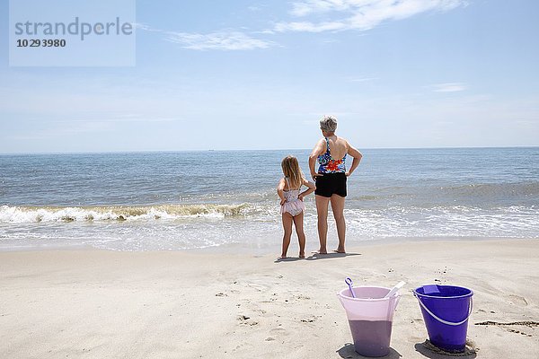 Seniorin mit Enkelin mit Händen auf der Hüfte und Blick vom Strand aus