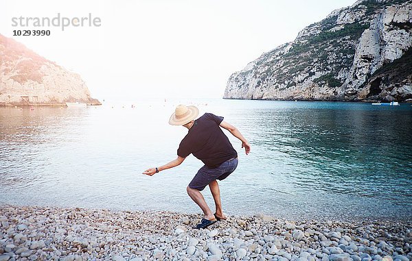 Rückansicht des jungen Mannes beim Abschöpfen von Steinen vom Strand  Javea  Spanien