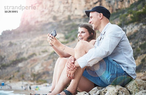 Erwachsener Mann und Teenager-Tochter beim Lesen von Smartphone-Texten am felsigen Strand  Javea  Spanien