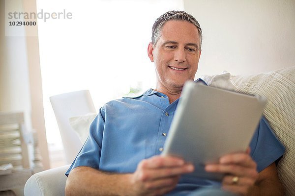 Erwachsener Mann liest digitales Tablett auf Sofa