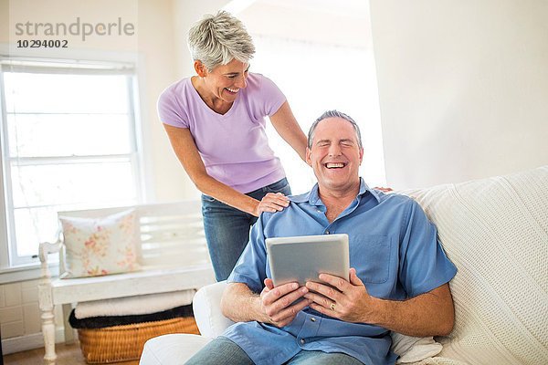 Reife Paare lachen bei der Benutzung des digitalen Tabletts