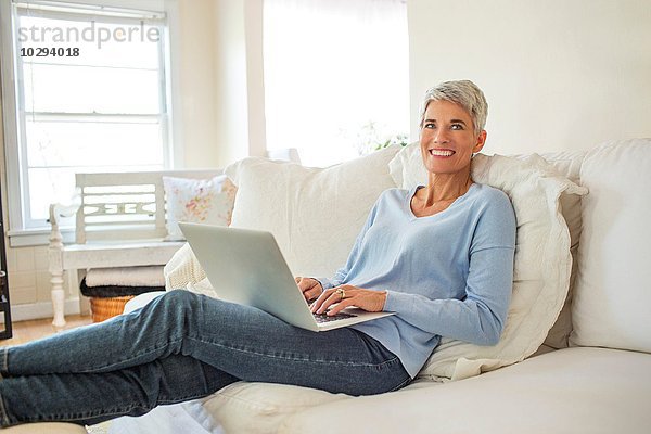 Portrait einer reifen Frau  die auf dem Sofa liegt und auf dem Laptop tippt