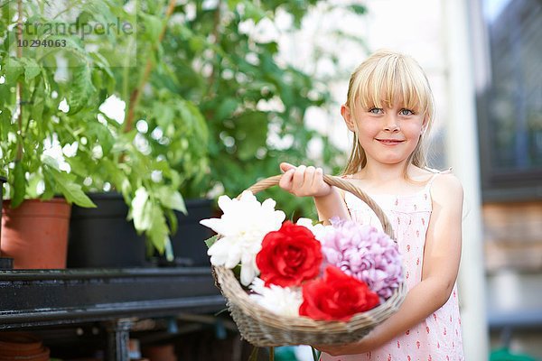 Süßes Mädchen hält frischen Blumenkorb im Gewächshaus