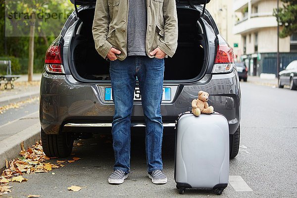 Mittlerer Erwachsener Mann steht neben dem Auto mit offenem Kofferraum  Koffer in der Straße