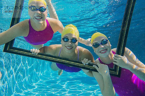 Drei Schwimmerinnen  unter Wasser  durch den Rahmen blickend