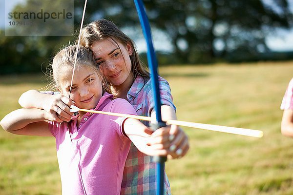 Mädchen lernen Bogenschießen von der Teenager-Schwester