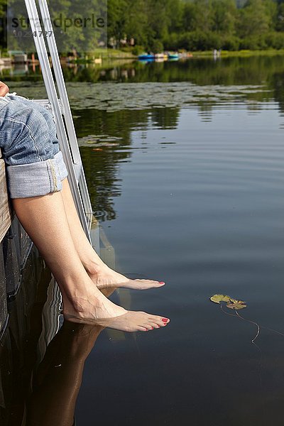 Nackte Füße einer Frau  die vom Pier aus im See baumelt.