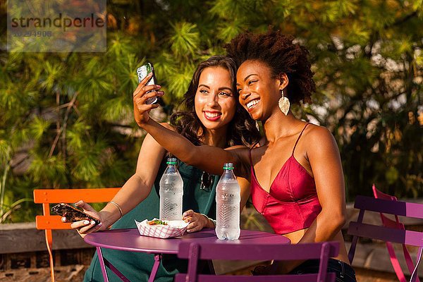 Junge Frauen nehmen Selfie auf die Bank