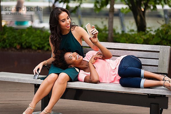Junge Frauen mit Smartphone auf der Parkbank