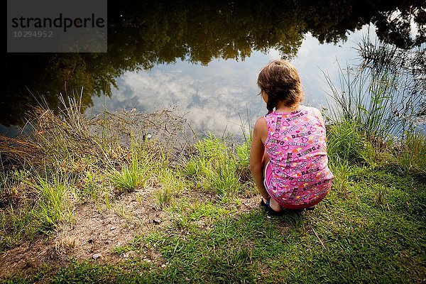 Rückansicht des Mädchens  das auf dem Flussufer hockt und Wasser sieht.
