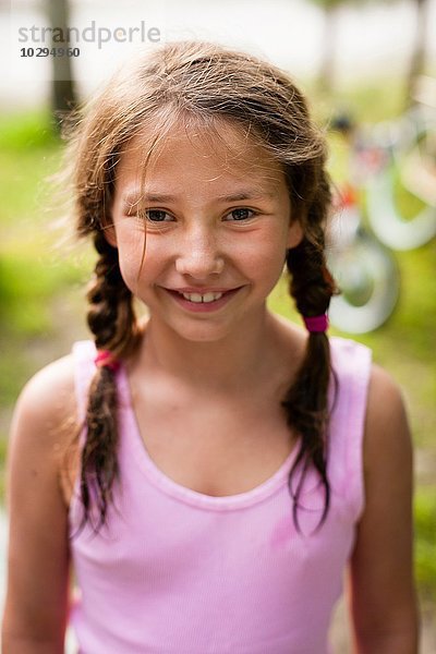 Hochwinkliges Porträt eines jungen Mädchens mit Zöpfen  das lächelnd in die Kamera schaut.