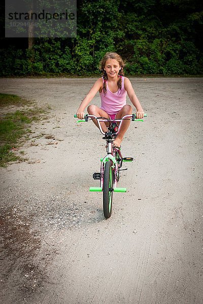 Vorderansicht des Mädchens  das auf dem Fahrrad balanciert  Beine hochgeklappt  Kamera lächelnd betrachtend