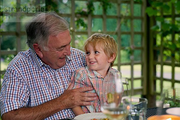 Enkel sitzt auf Großvaters Schoß  von Angesicht zu Angesicht lächelnd.