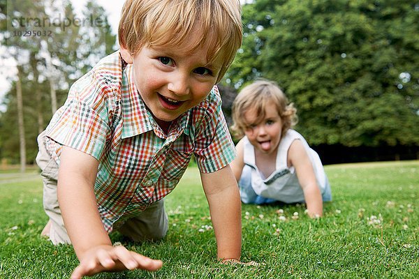 Junge und Mädchen auf Gras krabbeln auf Händen und Knien  die Kamera lächelnd betrachtend