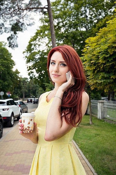 Junge Frau mit Kaffeetasse mit Smartphone auf der Straße