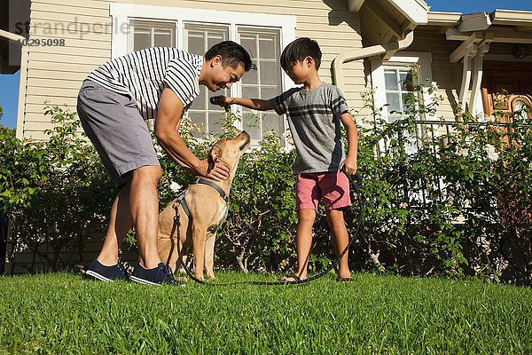 Vater und Sohn streicheln Hund im Garten