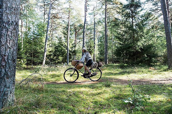 Reife Frau beim Radfahren mit Futterkörben im Wald