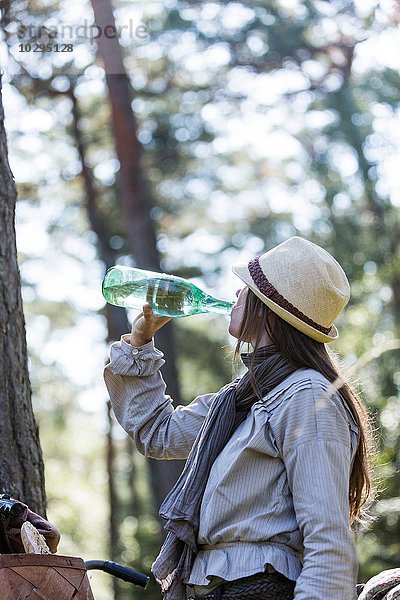 Reife Radfahrerin trinkt aus der Wasserflasche im Wald