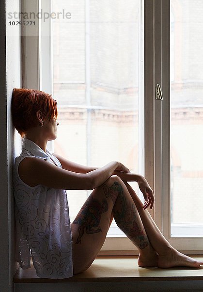 Seitenansicht der tätowierten mittleren erwachsenen Frau im Fenstersitz aus dem Fenster schauend