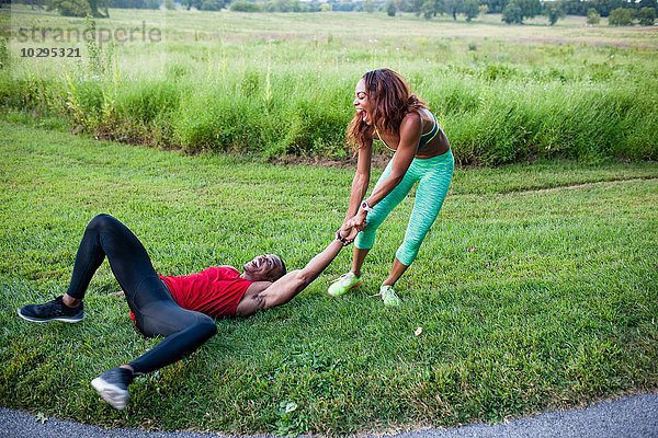 Junge Frau beim Training und Ziehen des Freundes auf Rasen
