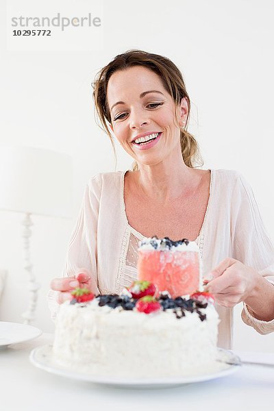 Reife Frau serviert fruchtbedeckten Kuchen mit lächelndem Blick nach unten