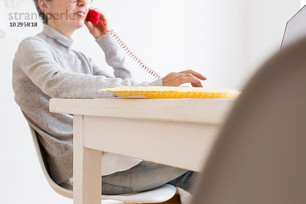 Schnittbild einer reifen Frau am Tisch mit Festnetztelefon  differenzierter Fokus