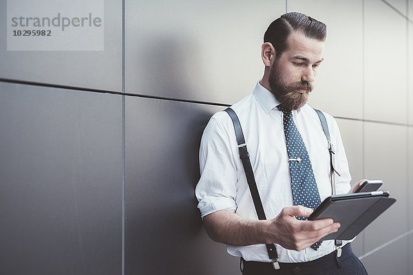 Stilvoller Geschäftsmann mit digitalem Tablett und Smartphone außerhalb des Büros