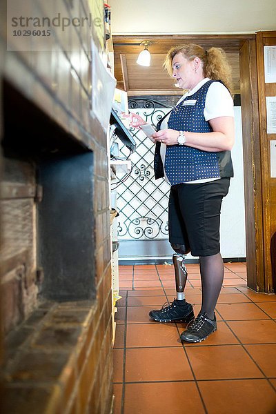 Mittlere erwachsene Frau mit Beinprothese  arbeitende Kasse im Restaurant