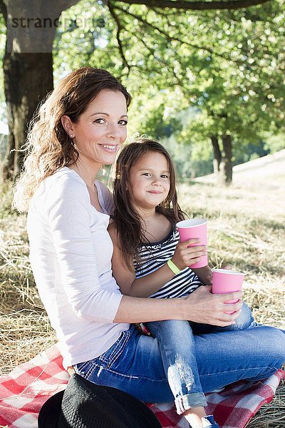 Porträt einer reifen Frau und Tochter beim Picknick aus Pappbechern