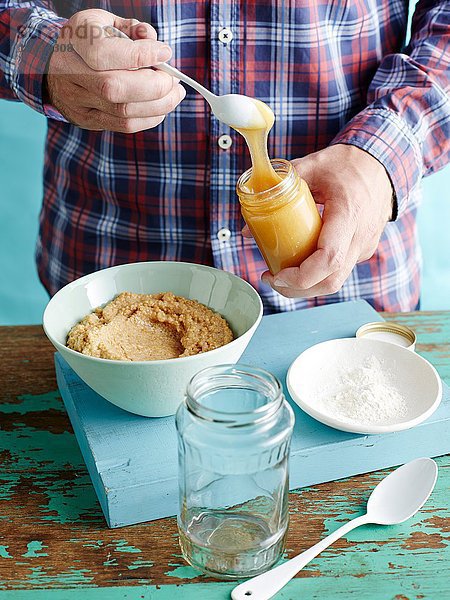 Mann bereitet frischen Senf Rezept Schritt 2  Hinzufügen von Honig zu gemischten Senfkörnern