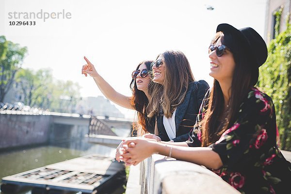 Drei stilvolle junge Freundinnen  die vom Flussufer der Stadt aufblicken.