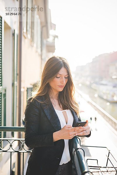 Junge Frau liest Smartphone-Texte auf Waterfront Balkon