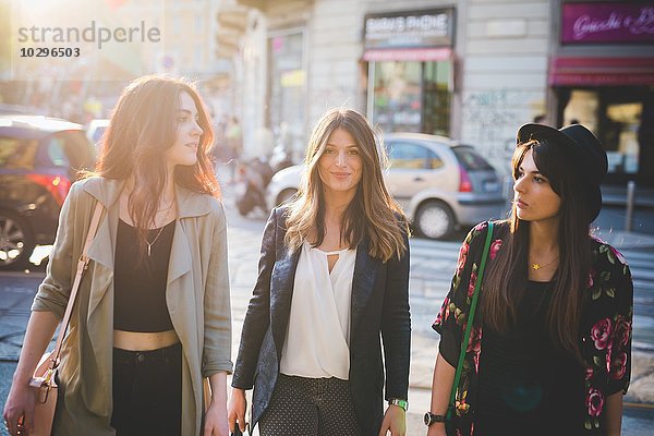 Drei junge Frauen  die auf der Straße spazieren gehen.