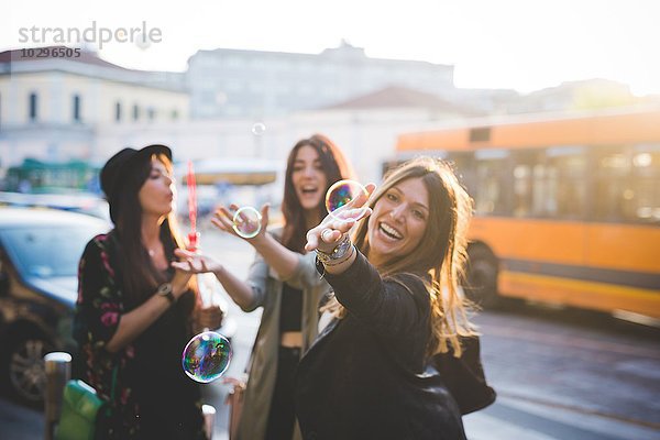 Drei junge Freundinnen blasen Blasen auf der Stadtstraße.